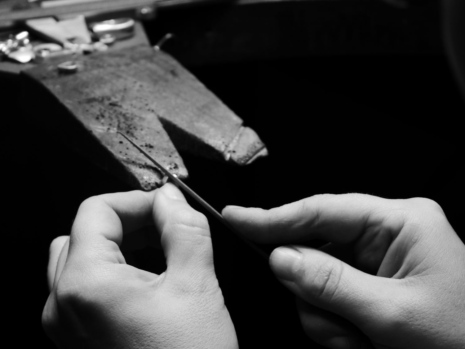 Two hands make jewellery at a jewellery bench.